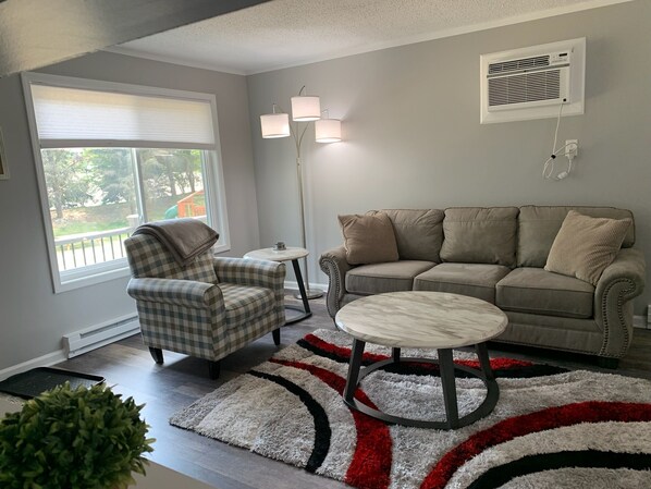 A living room with a checkered armchair, a beige sofa, a round coffee table, and a patterned rug. - Adventure Acres- Suite B1 (Holly)