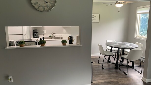 Een moderne keuken met een inbouwkookeiland, een eethoek met een ronde tafel en stoelen, en een wandklok.