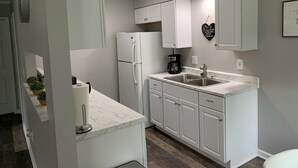 Een moderne keuken met witte kastjes, een marmeren aanrecht, een koelkast, een koffiezetapparaat en een hartvormig bord aan de muur.