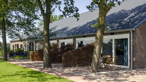 A modern building with large windows, a brick facade, and a covered outdoor seating area with chairs. - Group accommodation 32 pers, near Efteling and Beekse Bergen (Haghorst)