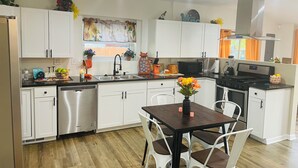 A modern kitchen with white cabinets, stainless steel appliances, and a wooden dining table with chairs.