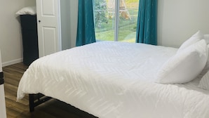 A bedroom with a bed, a window with curtains, a view of a playground, and a door.