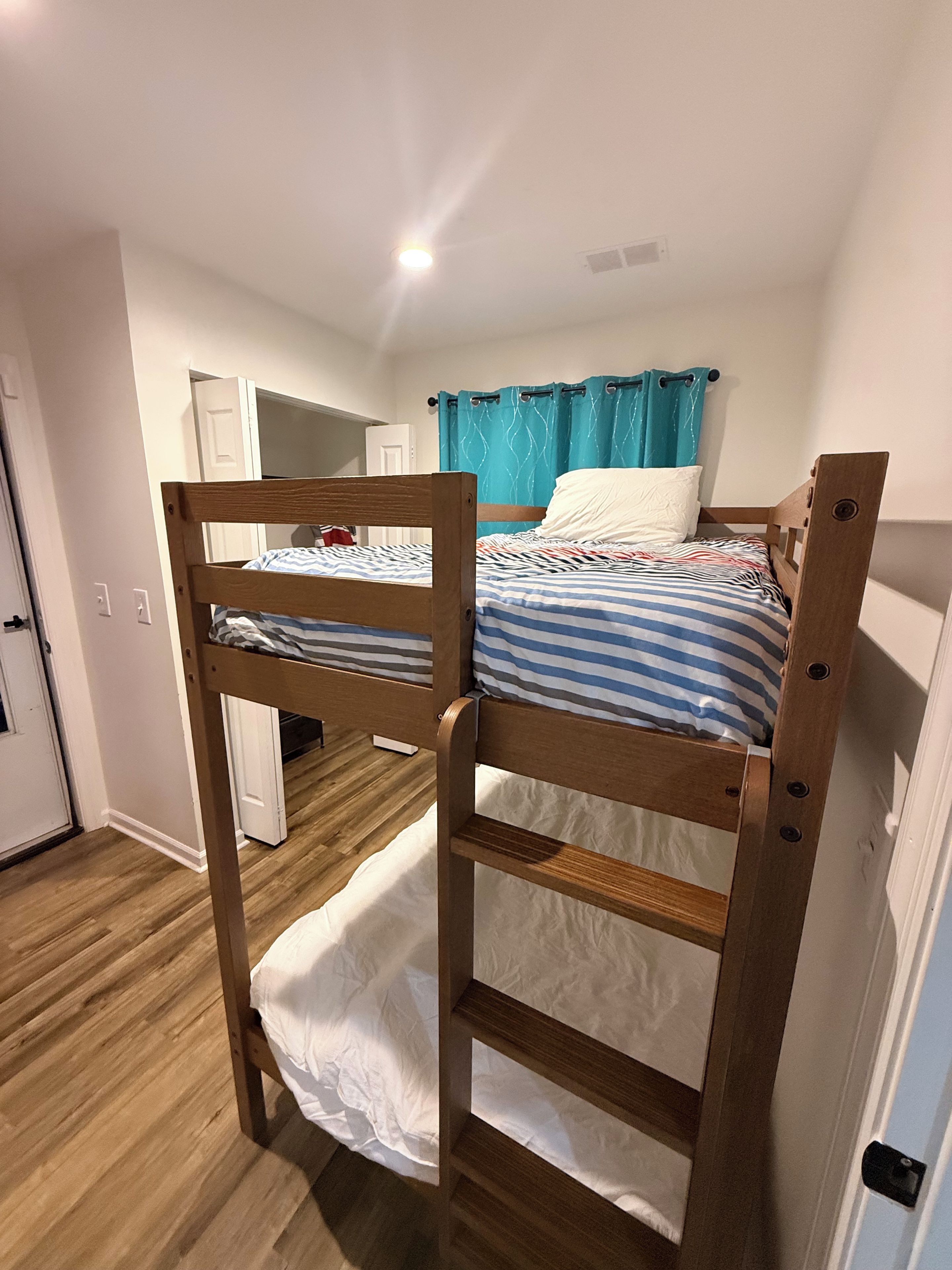 A room with two bunk beds, a door, a white wall, and a ceiling light.