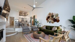 A spacious living room with a green sofa, striped armchairs, and a round coffee table. A wall-mounted hat collection adds a unique touch. - Stunning West End Home - Walkable Area (Nashville)