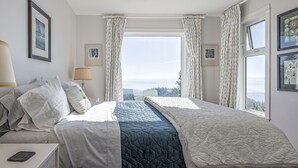 Et soveværelse med en stor seng, et natbord, en lampe og udsigt til det fri gennem et vindue.