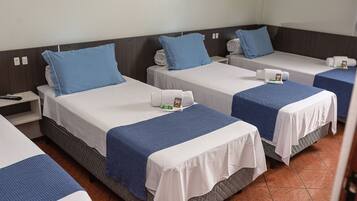 A hotel room with three single beds, each with a blue pillow and a white bedspread.