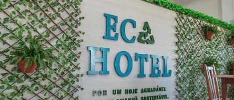 A sign for "EC HOTEL" with a green leafy wall design and potted plants.