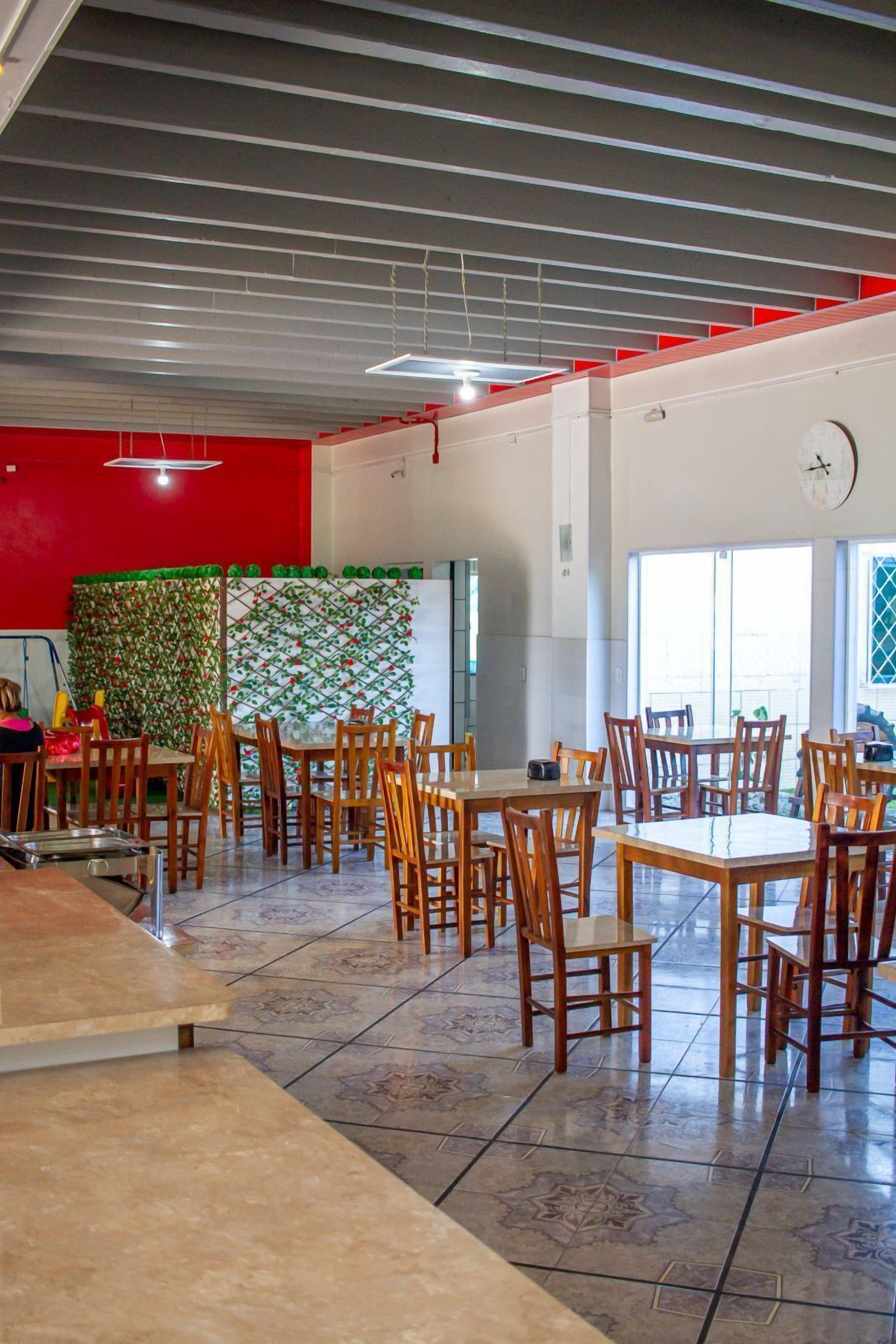 A spacious indoor dining area with multiple wooden tables and chairs, a tiled floor, and a red accent wall.
