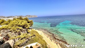 A coastal landscape with clear turquoise waters, a sandy beach, and a rocky cliff with dense greenery. - Maite Apartment in Moraira – Seafront holiday apartment for 4 guests with air conditioning and Wi-Fi (Moraira)