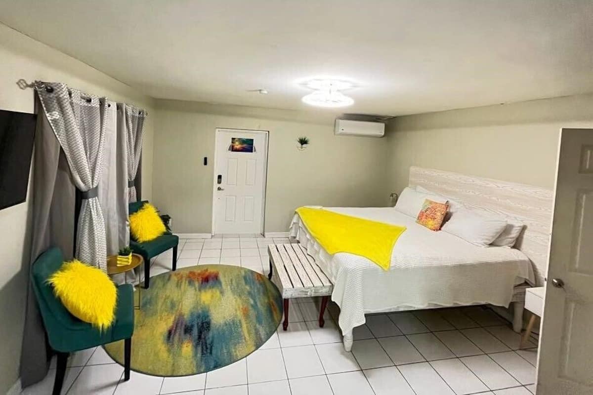 A room with a bed, two chairs, a small table, and a door.