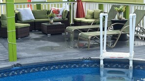 Uma área à beira da piscina com esquema de cores verde e branco, incluindo piscina, espreguiçadeiras e um espaço de estar com almofadas e uma mesa.