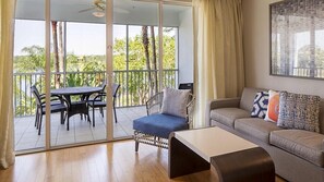 Relax in this stylish living room with a balcony offering views of palm trees and a clear sky.