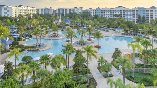 Ein Resort mit mehreren Schwimmbecken, Palmen und einer Reihe von Hotelgebäuden im Hintergrund.