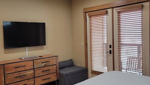 A bedroom with a bed, a TV on a wooden dresser, and a sliding door with blinds.