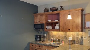 A kitchen with wooden cabinets, a granite countertop, a microwave, a coffee maker, and a hanging light fixture.