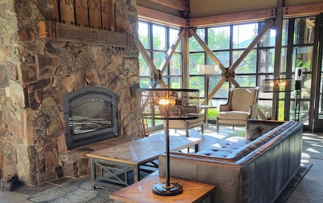 A stone fireplace, wooden beams, a cushioned bench, and a table with a lamp.