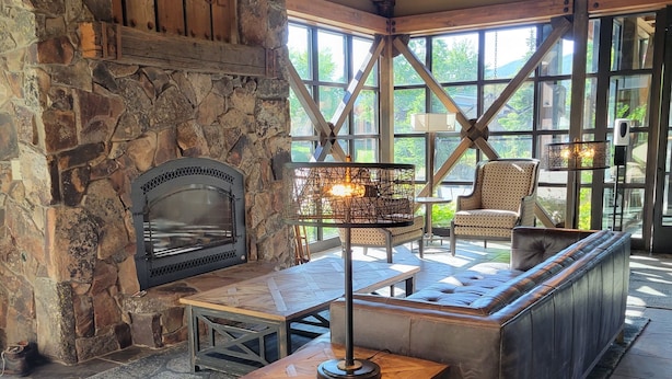 A stone fireplace, wooden beams, a cushioned bench, and a table with a lamp.