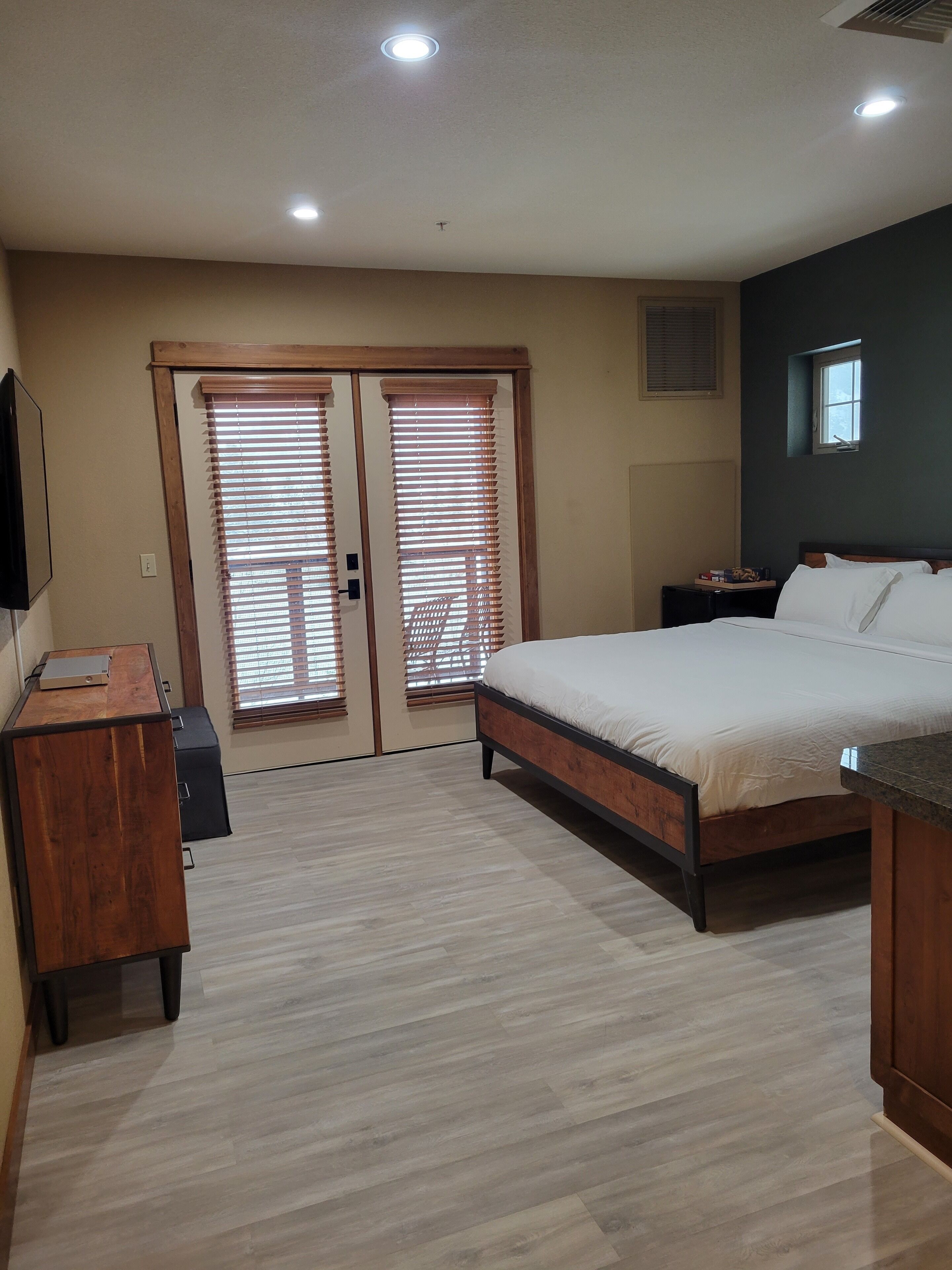 Een slaapkamer met een bed, een bureau, een dressoir en een raam met jaloezieën.