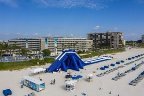 Un hôtel situé en bord de mer, composé de plusieurs bâtiments, doté d’un grand toboggan gonflable et de nombreuses chaises de plage.