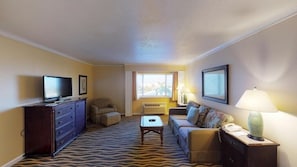 Une chambre d’hôtel équipée d’un téléviseur à écran plat, d’un canapé, d’une petite table, d’une commode et d’une lampe.