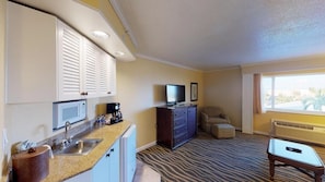 A compact hotel room with a kitchenette, a flat-screen TV, a sofa, and a large window.