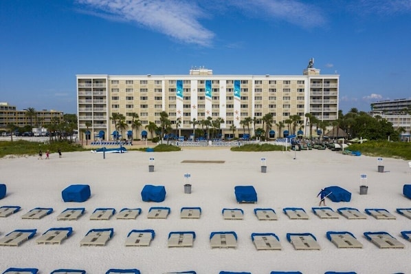 A hotel with a large building, a sandy beach in front, and rows of blue beach chairs.