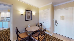 Une chambre d’hôtel dotée d’un coin repas comprenant une table ronde et quatre chaises, un tableau encadré au mur, et une porte avec une serrure et une clé dans la serrure.