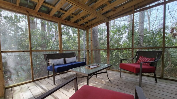 A covered outdoor seating area with a wooden deck, a glass table, and two chairs with cushions. - Blue Ridge Mountain Cottage~1 minute from Parkway! (Newland)