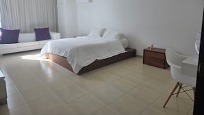 Quarto moderno com cama, mesa de cabeceira, cadeira, sofá e janela com cortinas.