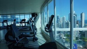 Uma academia com equipamentos de ginástica e uma grande janela com vista para a paisagem urbana.