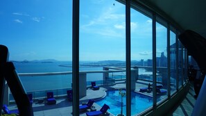 A modern hotel room with a large window overlooking a swimming pool and a cityscape. - Best Apartment, Ocean Front, High floor, Best PTY Location (Panamá)