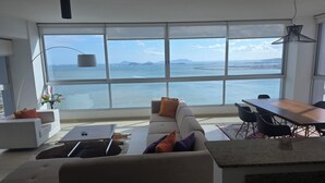 Uma sala de estar moderna com uma grande janela com vista para o mar, um sofá, uma mesa de centro e uma área de jantar.
