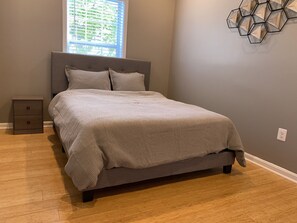 A bedroom with a bed, a nightstand, and a window with blinds. - An Eclectic Home for the World Traveler (Washington)