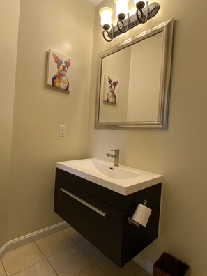 A bathroom with a white sink, dark cabinetry, a large mirror, and two wall-mounted light fixtures. - An Eclectic Home for the World Traveler (Washington)
