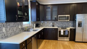 A modern kitchen with dark cabinets, a stainless steel refrigerator, a microwave, and an oven. - An Eclectic Home for the World Traveler (Washington)