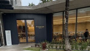 A modern building with a 'Premium Restaurante' sign, outdoor seating, and a well-maintained garden area.