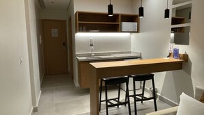 A compact kitchen with a central island, two bar stools, a white sofa, and a small seating area.