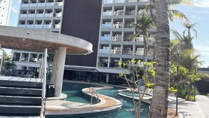 A modern hotel with a large pool area, palm trees, and a view of a tall building.