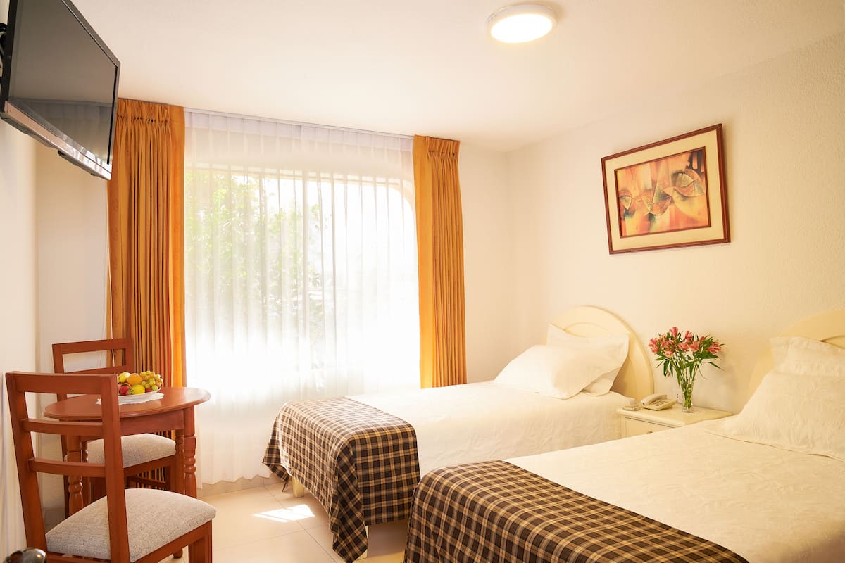 A hotel room with two beds, a dining table with chairs, a TV, and a painting on the wall.