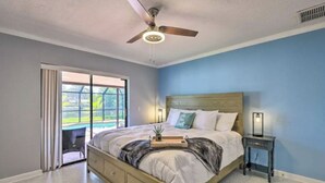 Ein Schlafzimmer mit Bett, Deckenventilator, Nachttisch und Blick auf einen Pool durch eine Schiebetür.