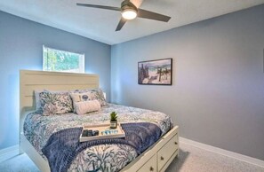 Quarto com cama, ventoinha no teto, janela e quadro na parede.