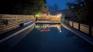 A swimming pool with a wooden deck, a red umbrella, and string lights. - Oliver Country House in the Wine Capital of Canada (Oliver)