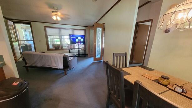 Een kamer met een bed, een televisie, een eettafel met stoelen en een prullenbak.