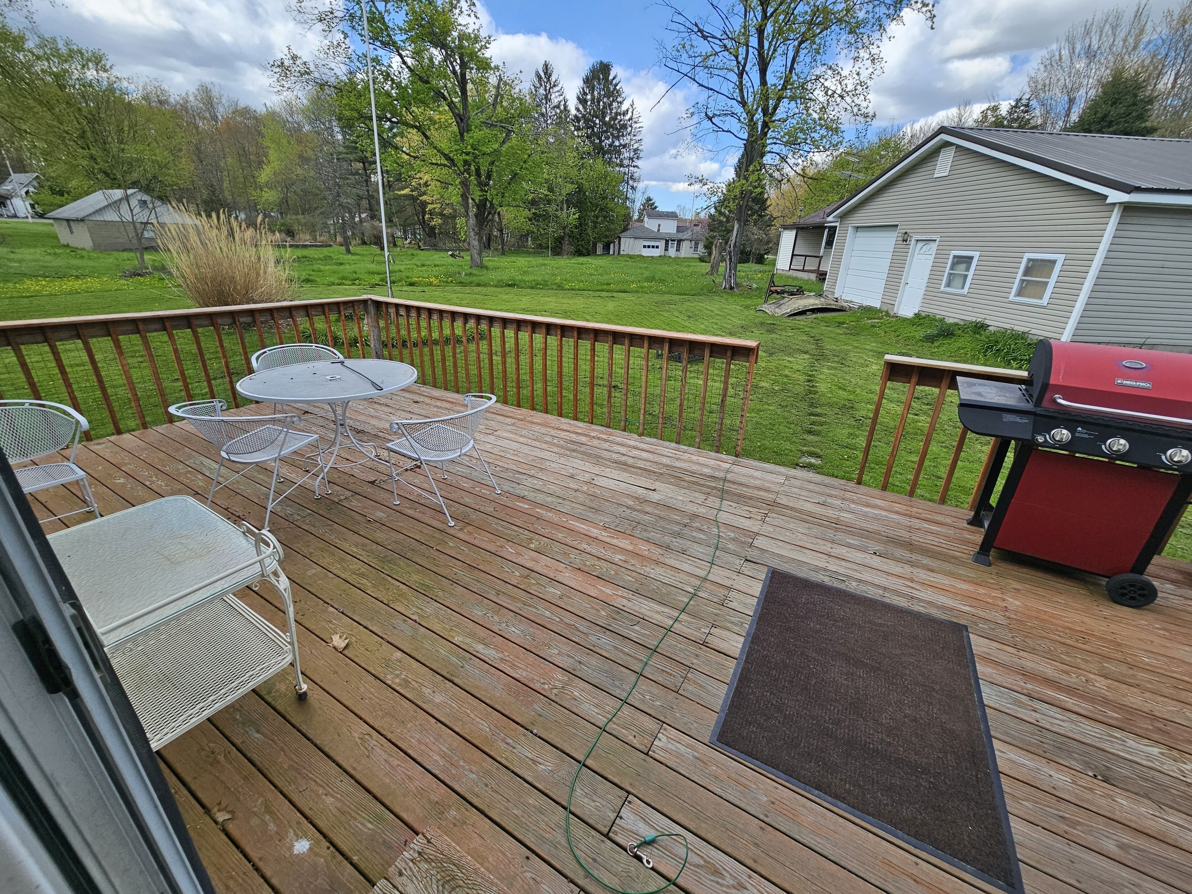 A wooden deck with a barbecue grill, outdoor seating, and a view of a grassy yard and houses.