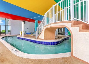 An indoor swimming pool with a tiled edge, a staircase, and a railing.
