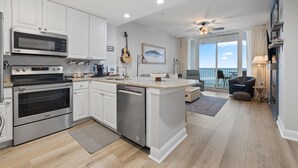 A modern kitchen with stainless steel appliances, a dishwasher, and a large island. There is a dining area with a view of the ocean. - Lighthouse 703 "Sea Haven" Beachfront condo with huge balcony! (Gulf Shores)