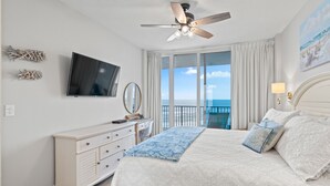 A bedroom with a bed, a ceiling fan, a TV, a dresser, a window with curtains, and a painting on the wall. - Lighthouse 703 "Sea Haven" Beachfront condo with huge balcony! (Gulf Shores)