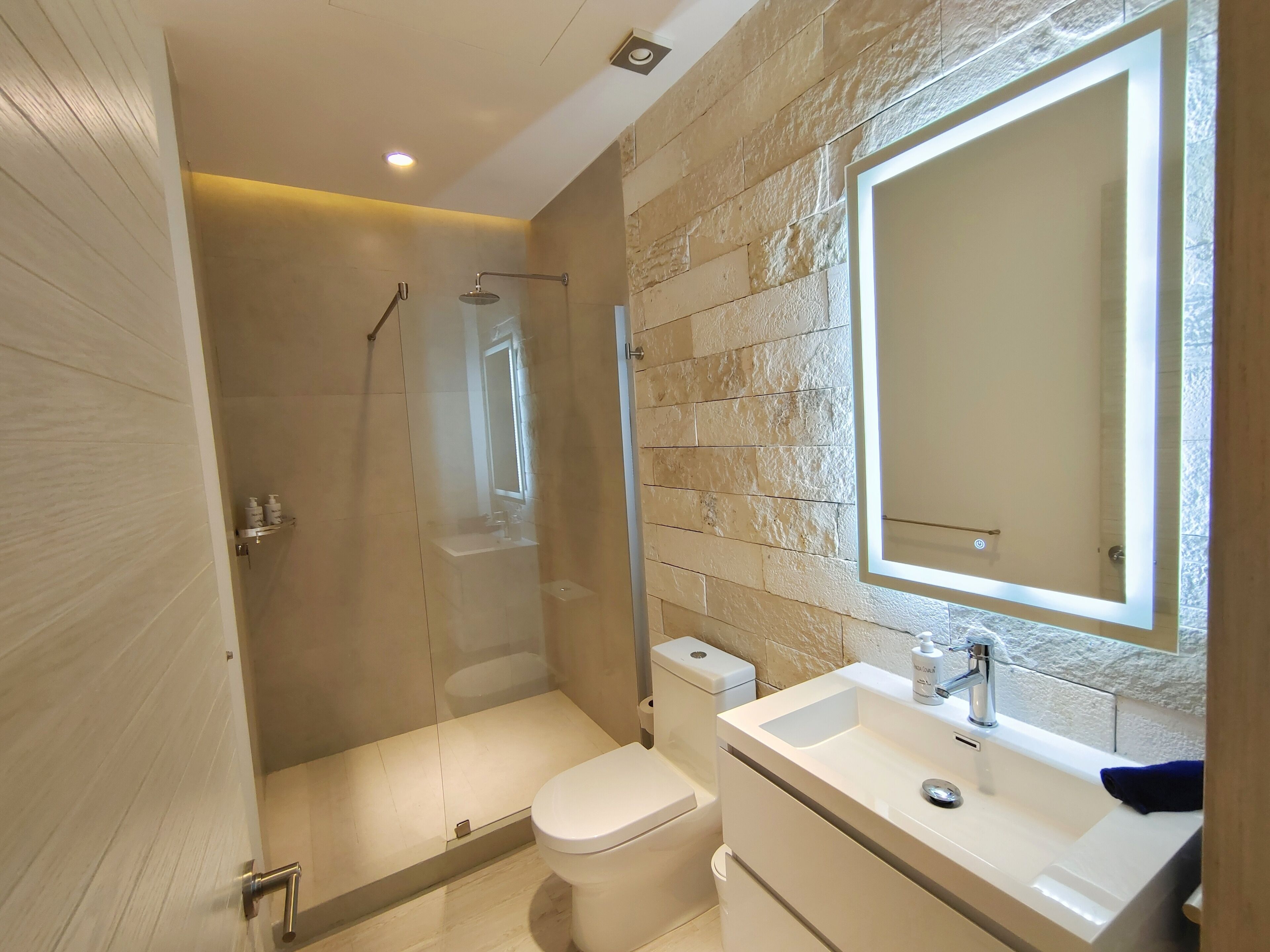 Un baño moderno con ducha envuelta en vidrio, inodoro y lavamanos con un espejo grande.
