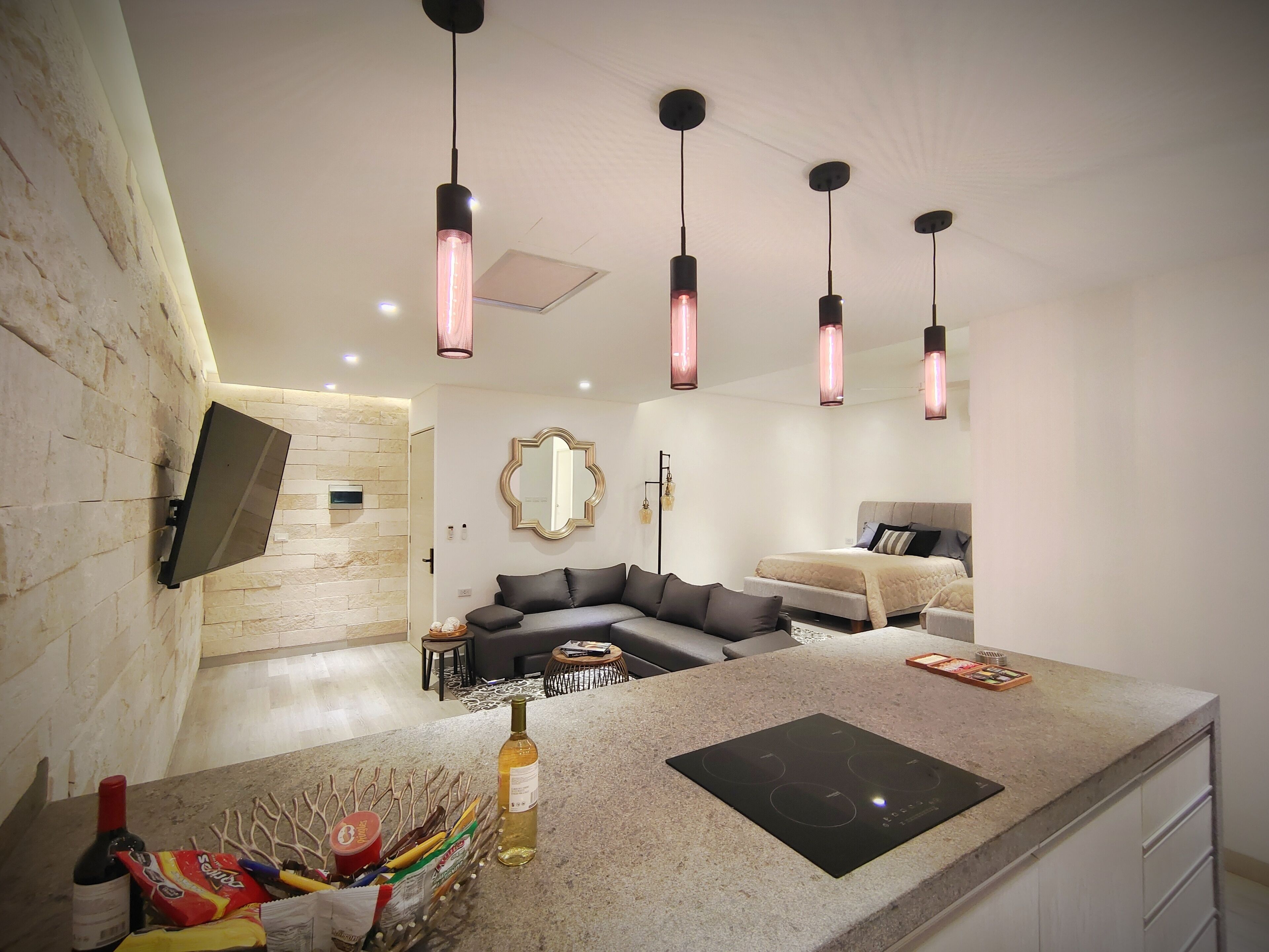 Uma sala de estar moderna com ilha de cozinha integrada, televisão de tela plana na parede, sofá e cama com cabeceira.