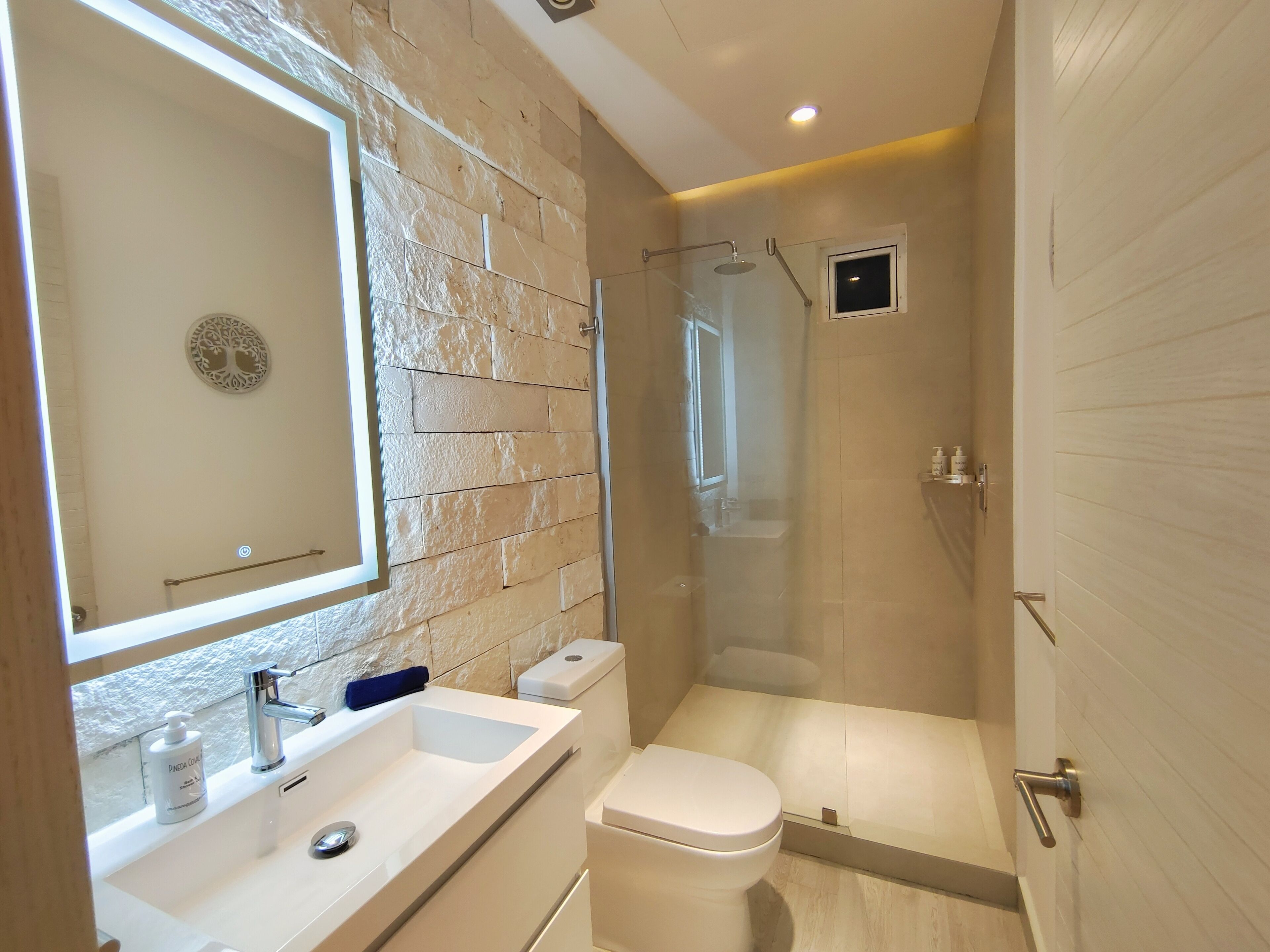 A modern bathroom with a stone wall, a large mirror, a sink with a faucet, a toilet, and a shower area.